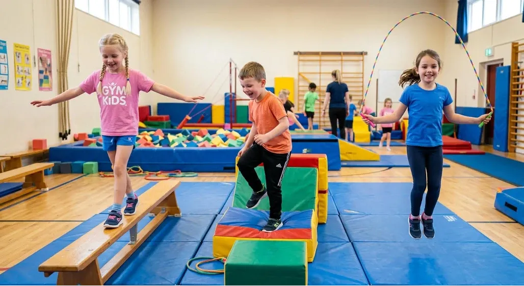 Bambini impegnati in un percorso motorio in palestra, tra materassi, moduli morbidi e trave di equilibrio.